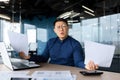 Worried Asian man sits in the office, holds documents in his hands. Spreads his hands Royalty Free Stock Photo