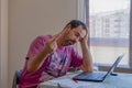 Worried bearded man dressed in a purple t-shirt looking at the laptop