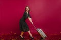 Worried beautiful girl in long vintage dress dragging big suitcase. Studio shot of tired caucasian woman in high heel