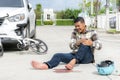 Worried biker holding his head and sitting on a pavement next to a car and bike crash, pedestrian crossing after accident Royalty Free Stock Photo