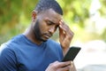 Worried black man checking smart phone in a park Royalty Free Stock Photo