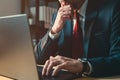 Worried businessman working on laptop computer late at night in dark office, thinking with hand on the chin