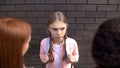 Worried caucasian schoolgirl looking at elder students, communication conflict