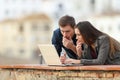 Worried couple checking news on a laptop in a terrace