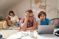 Worried father helping his little son with homework while mother and daughter sitting on sofa and playing with pazzles Royalty Free Stock Photo