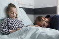 Worried father sitting next to ill little girl resting on patient bed Royalty Free Stock Photo