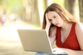 Worried female checking laptop in a park