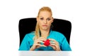 Worried female doctor or nurse sitting behind the desk and holding heart model Royalty Free Stock Photo