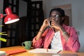 Worried frustrated African student guy making call, talking on mobile phone while studying at home Royalty Free Stock Photo