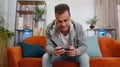 Worried funny young man boy playing shooter online video games celebrate win on smartphone at home