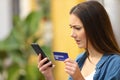 Worried girl paying with credit card and smart phone outdoors