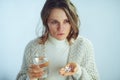 Worried housewife with cup of water holding many pills