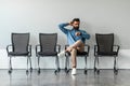 Worried indian job seeker waiting for interview far too long, sitting on chair alone in row, checking time Royalty Free Stock Photo