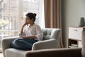 Worried Indian woman sit on armchair looks aside, feels concerned