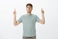 Worried intense funny fair-haired guy in t-shirt, pointing up with raised index fingers and looking at sky with anxious