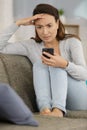 Worried lady on sofa in front smartphone