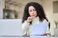 Worried latin business woman holding documents working with laptop. Royalty Free Stock Photo