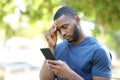 Worried man with black skin checking mobile phone in a park Royalty Free Stock Photo