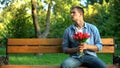 Worried man with bunch of tulips waiting girlfriend for date on bench in park