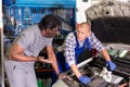 Worried client talking with specialist about repairing his car engine at workshop Royalty Free Stock Photo