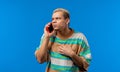 Worried man heard bad unexpected news by mobile phone conversation. Disappointed angry guy on blue background. Shock Royalty Free Stock Photo