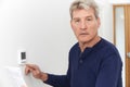 Worried Mature Man With Bill Turning Down Central Heating Thermostat