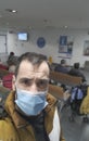 Worried middle-aged man with black hair and eyes wearing blue surgical mask in the waiting room of a hospital in Madrid, Spain