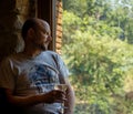 Worried middle-aged man with a glass of white wine in his hand illuminated by a dim evening light looking out a window of a rural Royalty Free Stock Photo