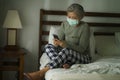 Worried middle aged woman 50s with grey hair and protective mask checking online news with mobile phone during covid-19 virus home Royalty Free Stock Photo