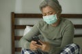 Worried middle aged woman 50s with grey hair and protective mask checking online news with mobile phone during covid-19 virus home Royalty Free Stock Photo