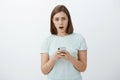 Worried nervous girl asking advice from friend trying text guy she loves standing concerned and troubled over white wall