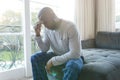 Worried, sad african american man thinking, sitting on couch holding head in living room Royalty Free Stock Photo