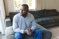 Worried, sad african american man thinking, sitting on couch looking out of window in living room Royalty Free Stock Photo