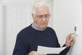 Worried Senior Man With Bill Turning Down Central Heating Thermo Royalty Free Stock Photo