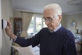 Worried Senior Man With Bill Turning Down Central Heating Thermostat At Home In Energy Crisis Royalty Free Stock Photo