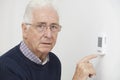 Worried Senior Man Turning Down Central Heating Thermostat