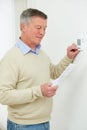 Worried Senior Man Turning Down Central Heating Thermostat Royalty Free Stock Photo