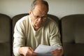 Worried senior man in white sweater and glasses reading utility bill in period of energy crisis. High heating prices. Royalty Free Stock Photo