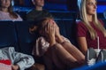 Worried small girl with mother covering eyes in the cinema while watching film.