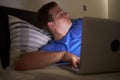 Worried Teenage Boy Using Laptop In Bed At Night