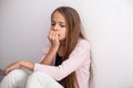 Worried teenage girl biting her nails sitting on the floor by th