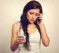 Worried unhappy young woman talking on one mobile phone and typing sms looking on two mobile phone. Vintage toned portrait