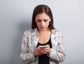 Worried unhappy young woman typing sms and looking on mobile phone
