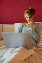 Worried woman sitting on bed at home, frowning and watching laptop computer, browsing on Internet. Royalty Free Stock Photo