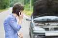 Worried woman talks on the phone near her old broken car on the road Royalty Free Stock Photo