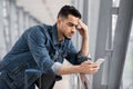 Worried young arab man looking at smartphone screen while waiting at airport