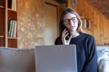 Worried young brunette woman talking on the smartphone in front of the laptop sitting on the sofa at home Royalty Free Stock Photo