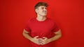 Worried young hispanic man, suffering from severe stomach ache, standing all alone over the isolated red background - an unhappy Royalty Free Stock Photo