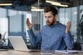 Worried young male businessman sits at the desk in the office and looks shocked at the laptop screen, throws up his Royalty Free Stock Photo