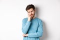 Worried young man with beard in sweatshirt, looking away pensive and thinking, standing troubled against white